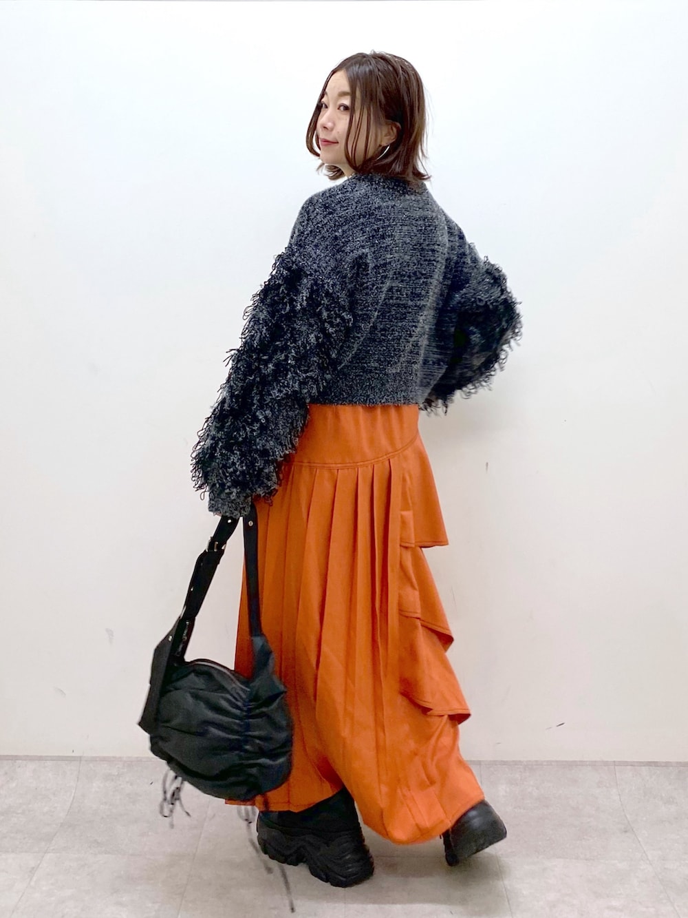 ブラック系のニット/セーター、オレンジ系のスカート、ブラック系のショルダーバッグを着用したレディースの冬コーディネートの6枚目の写真