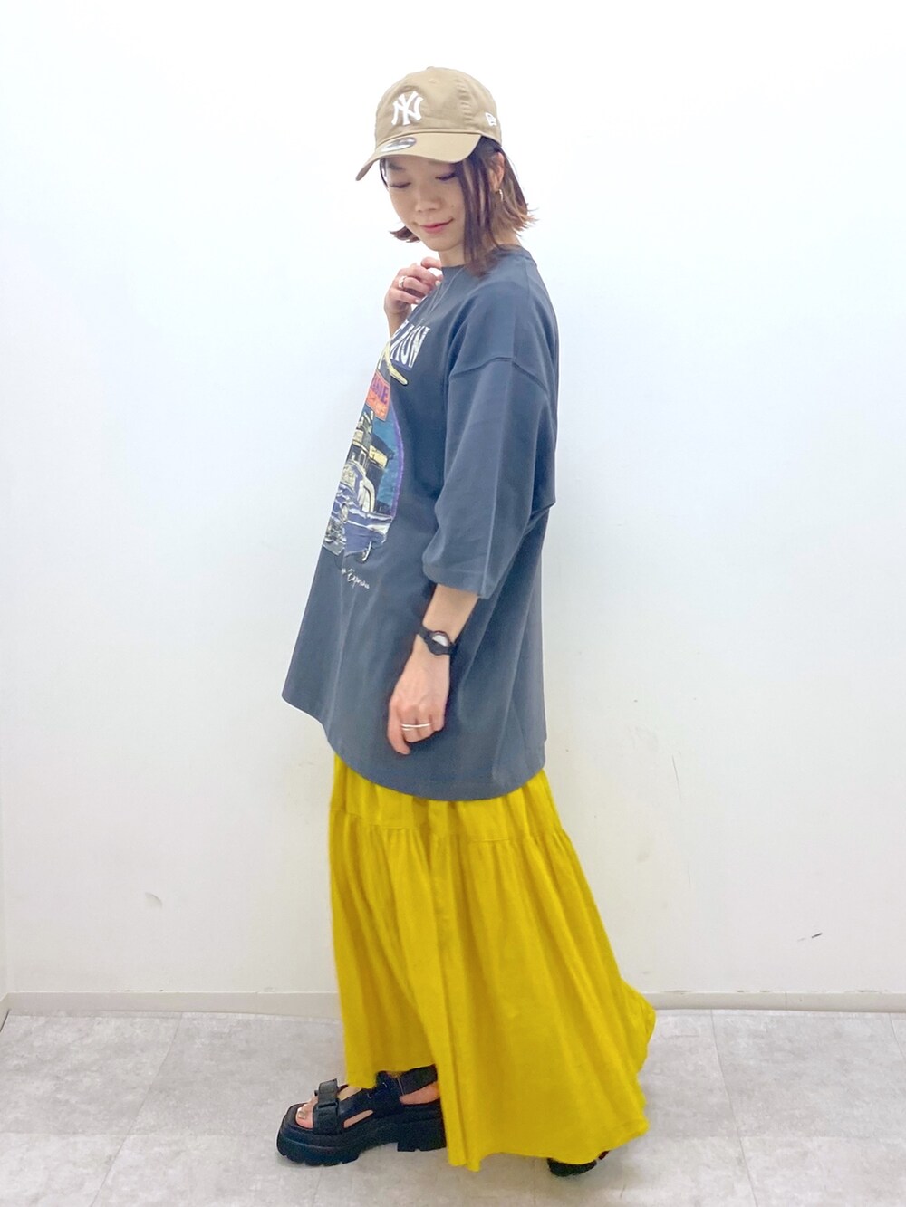 グレー系のTシャツ/カットソー、イエロー系のスカート、ブラック系のサンダルを着用したレディースの夏コーディネートの2枚目の写真