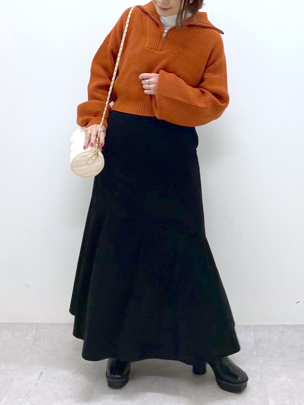 ブラック系のスカート、ホワイト系のバッグ、オレンジ系のニット/セーターを着用したレディースの秋コーディネートの4枚目の写真