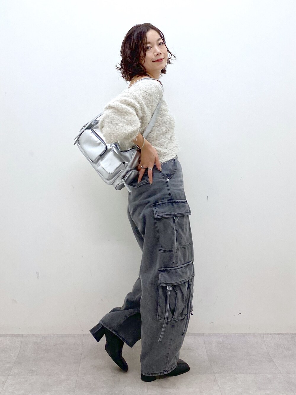 ブラック系のデニムパンツ、ブラック系のブーツ、シルバー系のショルダーバッグを着用したレディースの秋コーディネートの5枚目の写真