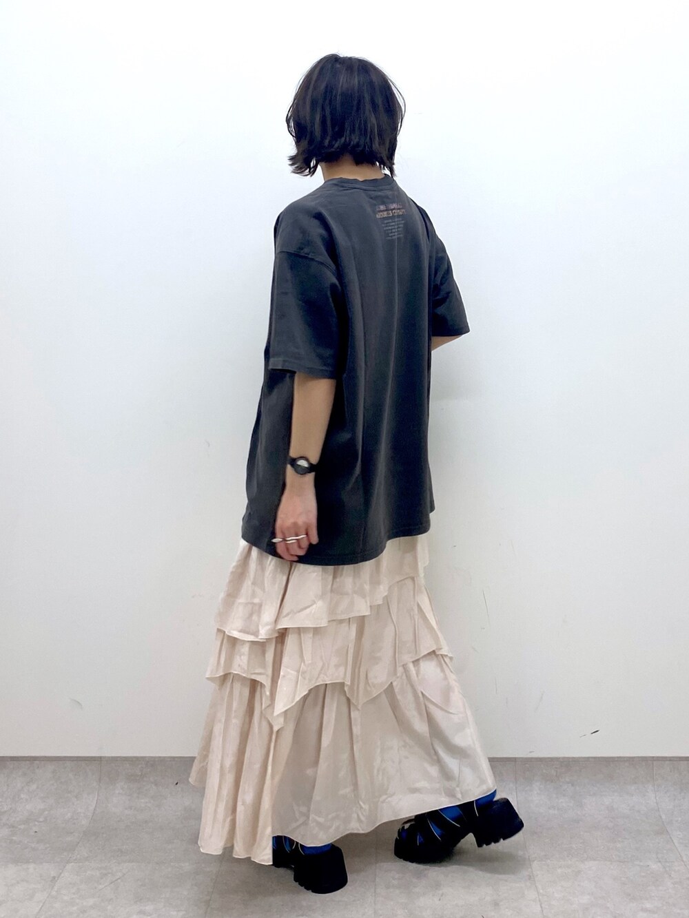 グレー系のTシャツ/カットソー、ホワイト系のスカート、ブラック系のサンダルを着用したレディースの春コーディネートの2枚目の写真