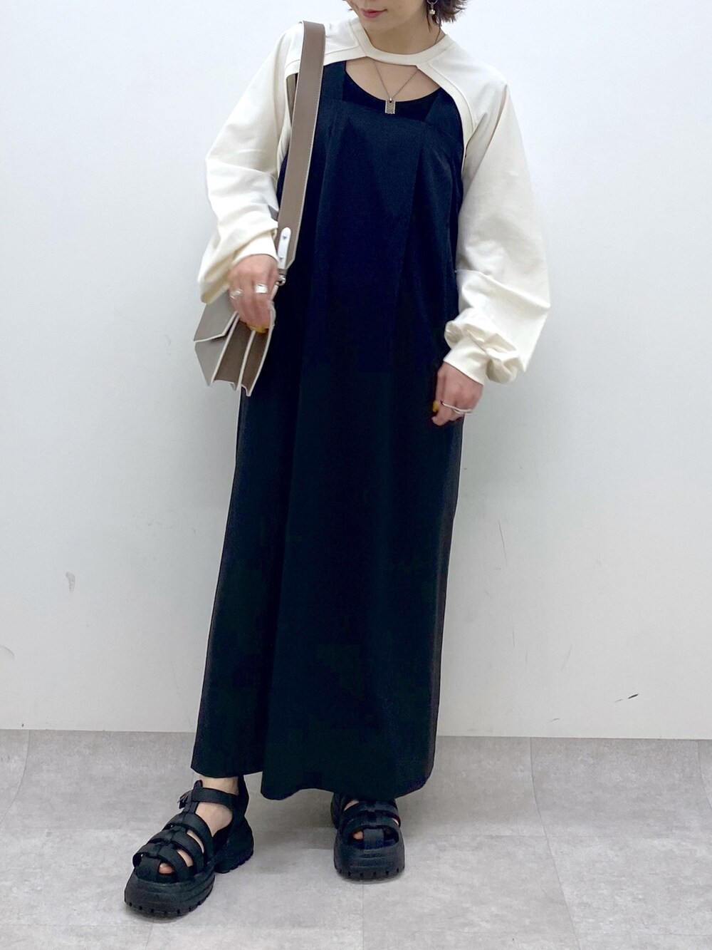 ブラック系のジャンパースカート、ホワイト系のTシャツ/カットソー、ブラウン系のショルダーバッグを着用したレディースの春コーディネートの5枚目の写真