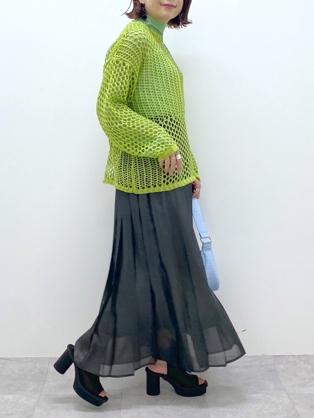 グリーン系のニット/セーター、グリーン系のTシャツ/カットソー、ブラック系のスカートを着用したレディースの春コーディネートの4枚目の写真