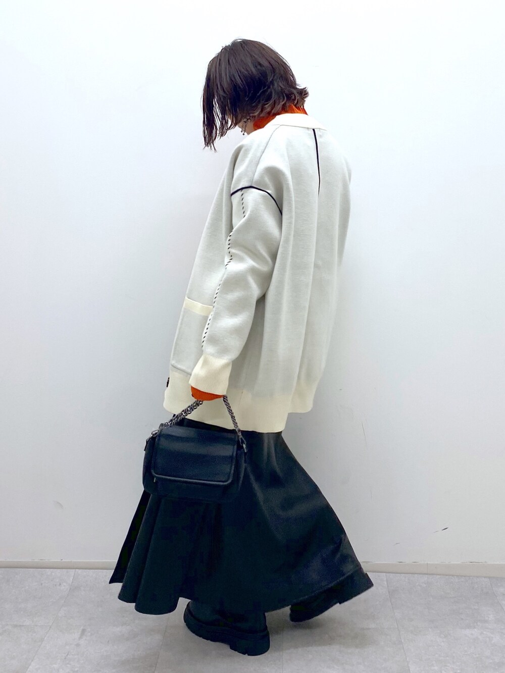 ブラック系のスカート、ブラック系のバッグ、オレンジ系のトップスを着用したレディースの秋コーディネートの3枚目の写真