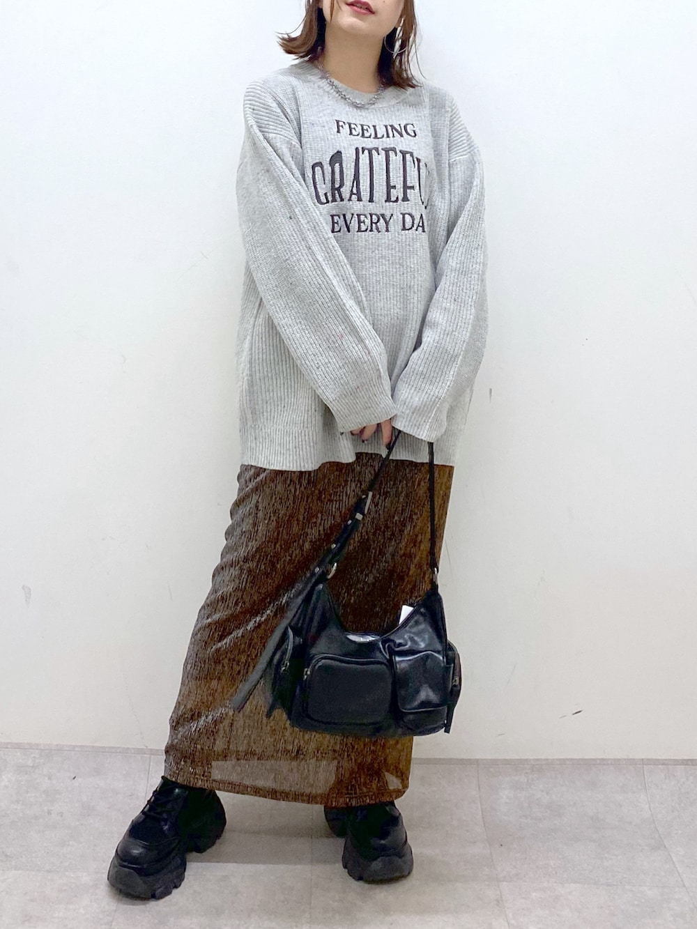 グレー系のニット/セーター、ゴールド系のスカート、ブラック系のショルダーバッグを着用したレディースの冬コーディネートの3枚目の写真