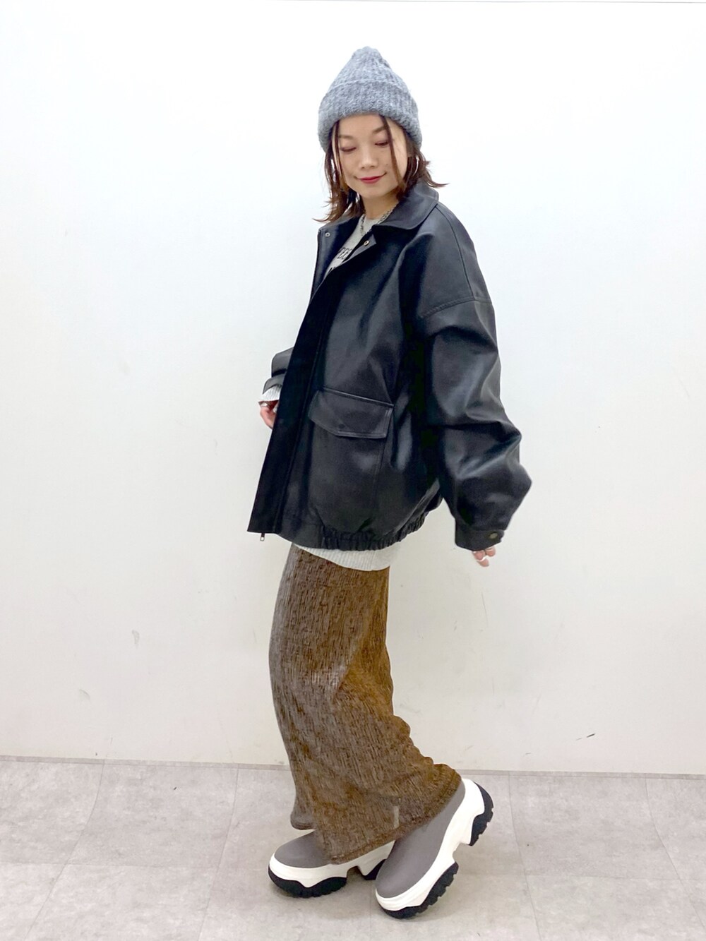 グレー系のニット/セーター、ブラック系のブルゾン、ゴールド系のスカートを着用したレディースの秋コーディネートの8枚目の写真