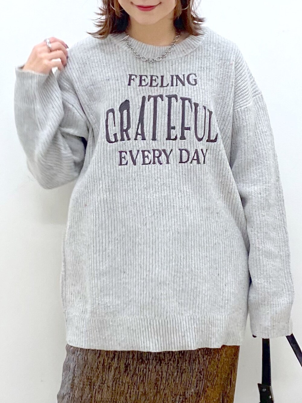 グレー系のニット/セーター、ゴールド系のスカート、ブラック系のショルダーバッグを着用したレディースの冬コーディネートの2枚目の写真