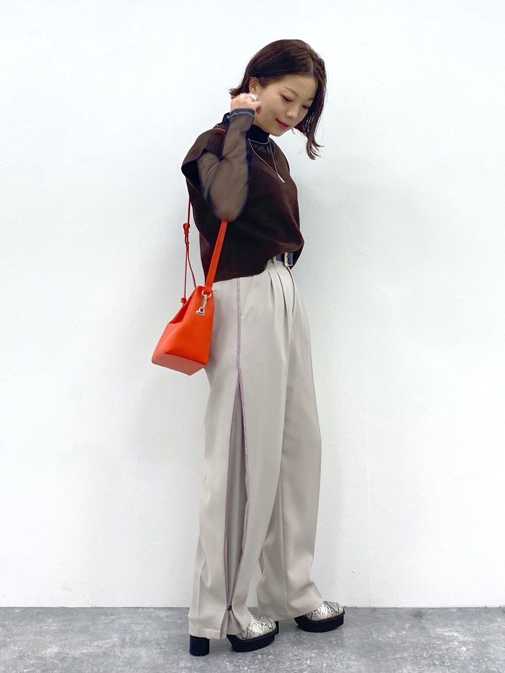 ベージュ系のスラックス、オレンジ系のショルダーバッグ、ブラウン系のワンピースを着用したレディースの夏コーディネートの2枚目の写真