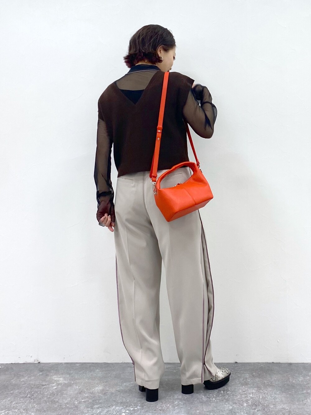 ベージュ系のスラックス、オレンジ系のショルダーバッグ、ブラウン系のワンピースを着用したレディースの夏コーディネートの3枚目の写真