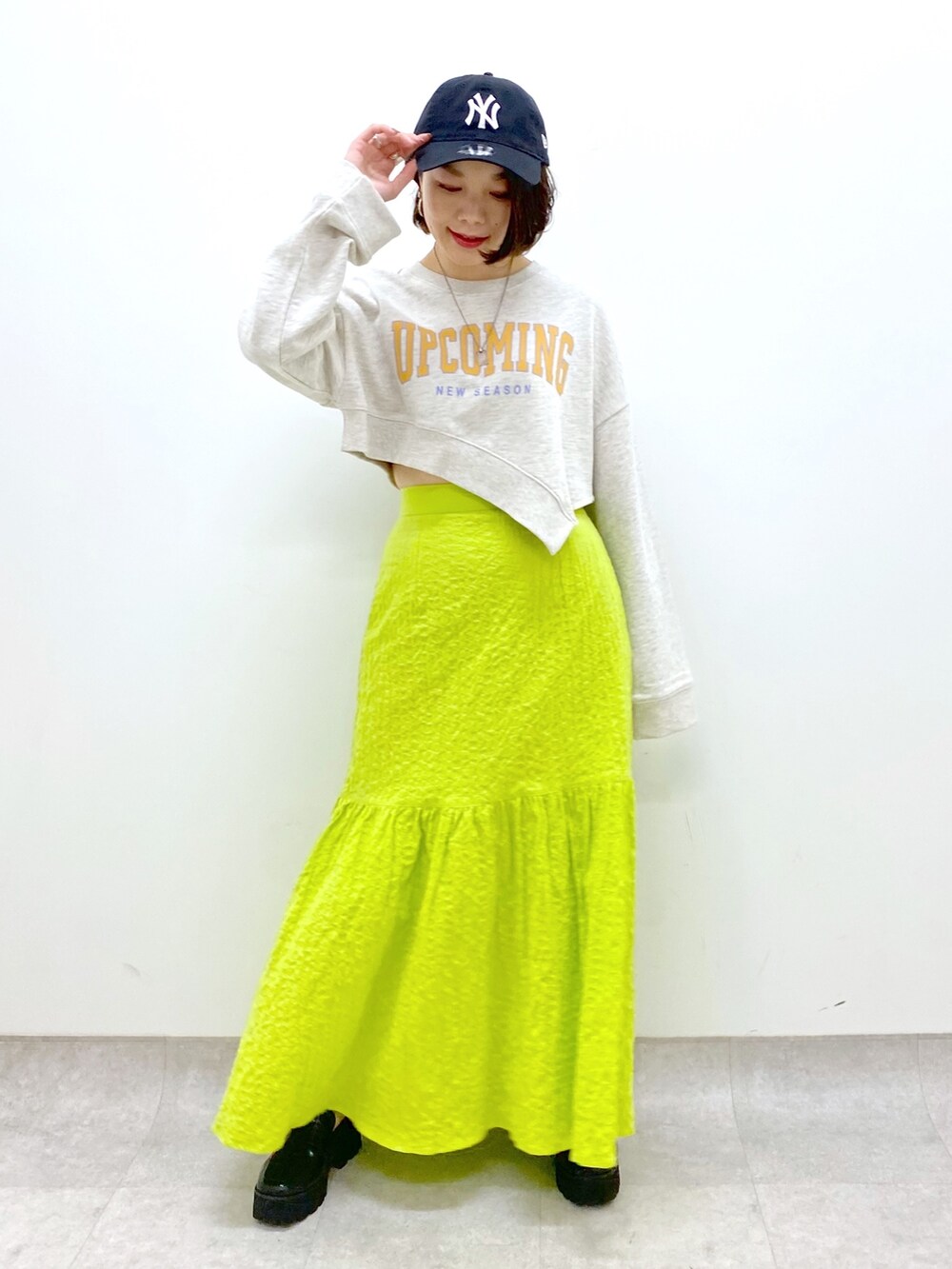 イエロー系のスカート、ベージュ系のトップス、ブラック系のローファーを着用したレディースの春コーディネートの2枚目の写真