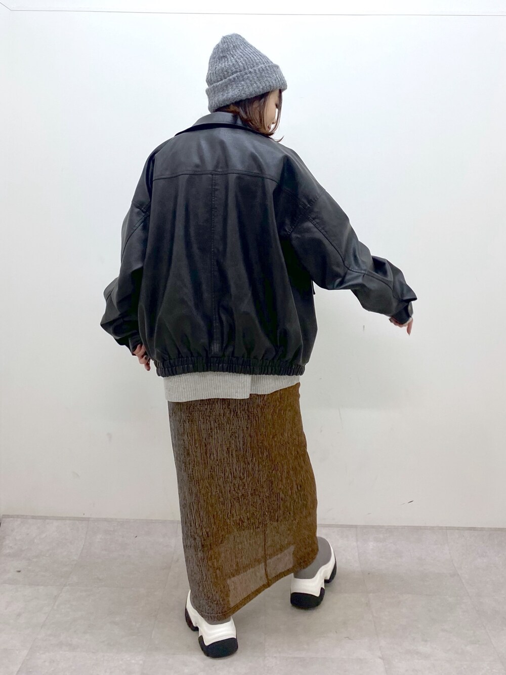 グレー系のニット/セーター、ブラック系のブルゾン、ゴールド系のスカートを着用したレディースの秋コーディネートの7枚目の写真