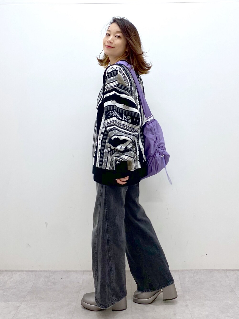 ブラック系のニット/セーター、ブラック系のデニムパンツ、パープル系のショルダーバッグを着用したレディースの秋コーディネートの6枚目の写真