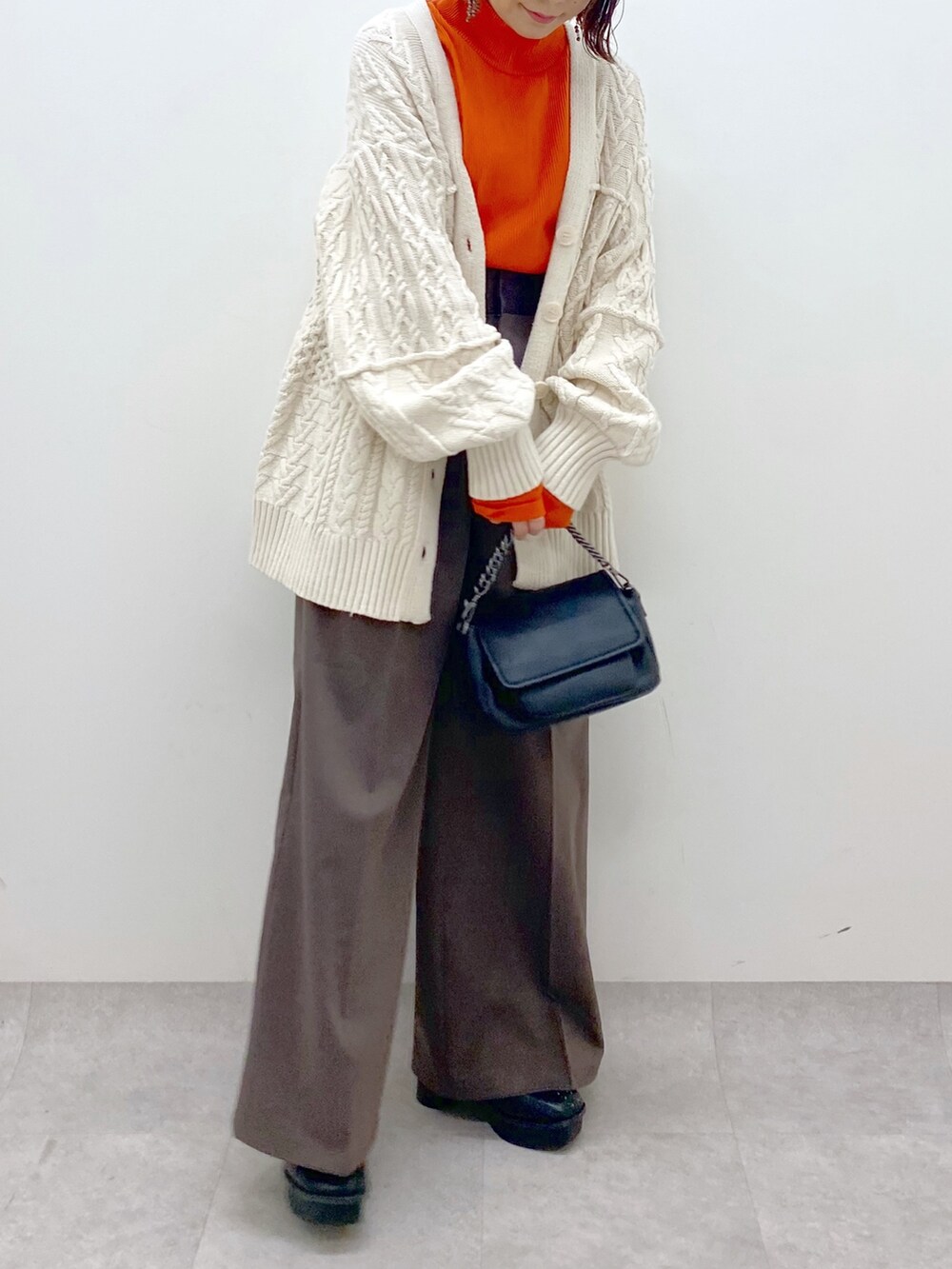 オレンジ系のトップス、ブラック系のバッグ、ブラック系のブーツを着用したレディースの秋コーディネートの4枚目の写真