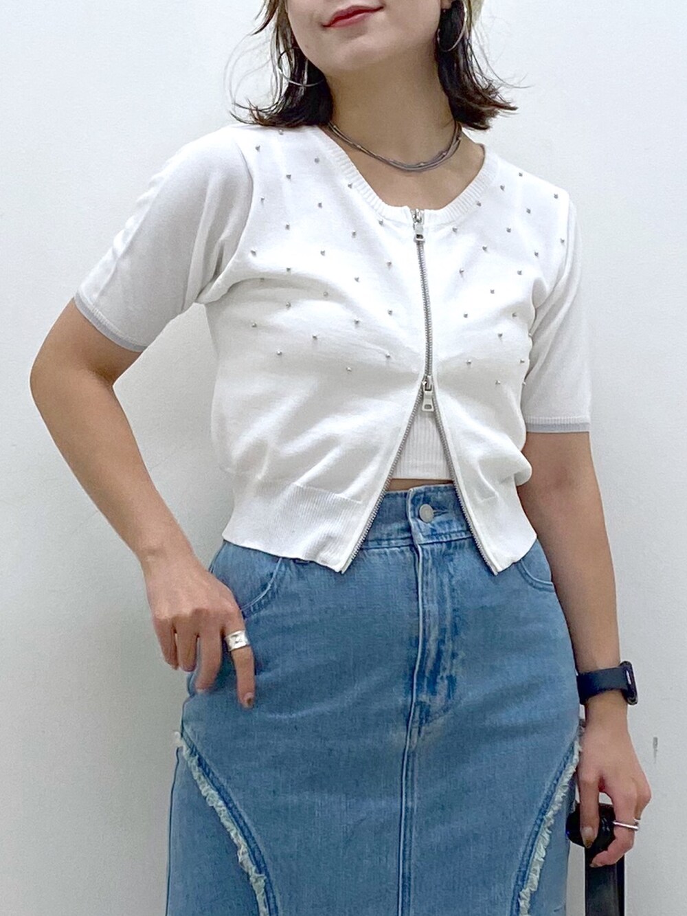 ブルー系のデニムスカート、ホワイト系のニット/セーター、ブラック系のショルダーバッグを着用したレディースの夏コーディネートの2枚目の写真