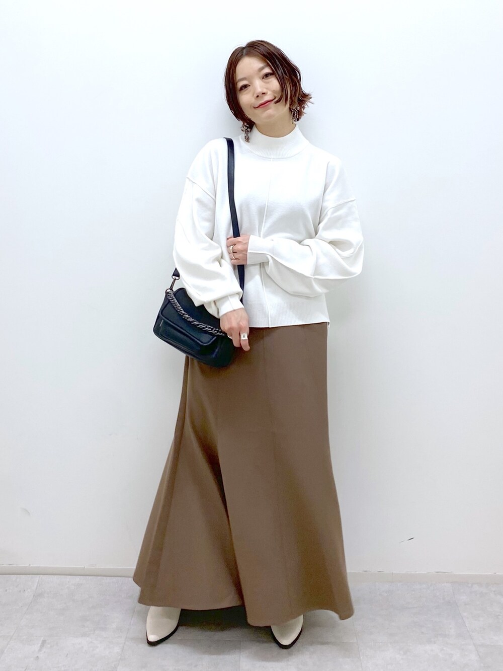 ホワイト系のブーツ、ブラウン系のスカート、ブラック系のバッグを着用したレディースの秋コーディネートの2枚目の写真