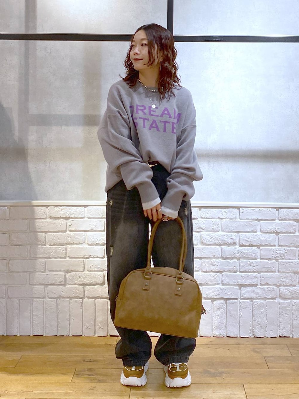 ベージュ系のスニーカー、イエロー系のボストンバッグ、ブラック系のデニムパンツを着用したレディースの秋コーディネートの4枚目の写真