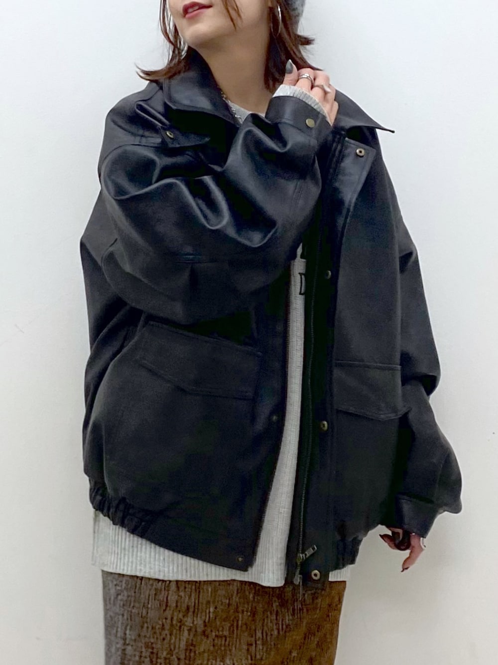 グレー系のニット/セーター、ブラック系のブルゾン、ゴールド系のスカートを着用したレディースの秋コーディネートの2枚目の写真