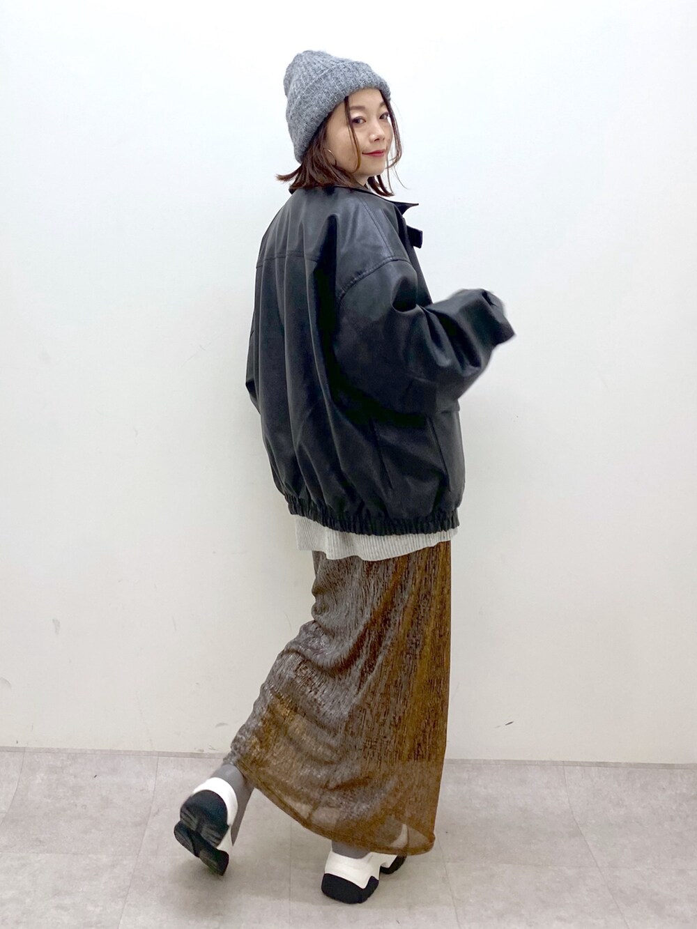 グレー系のニット/セーター、ブラック系のブルゾン、ゴールド系のスカートを着用したレディースの秋コーディネートの6枚目の写真