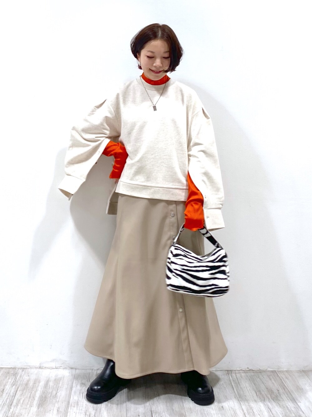 ブラウン系のスカート、ブラック系のバッグ、ベージュ系のトップスを着用したレディースの夏コーディネートの2枚目の写真