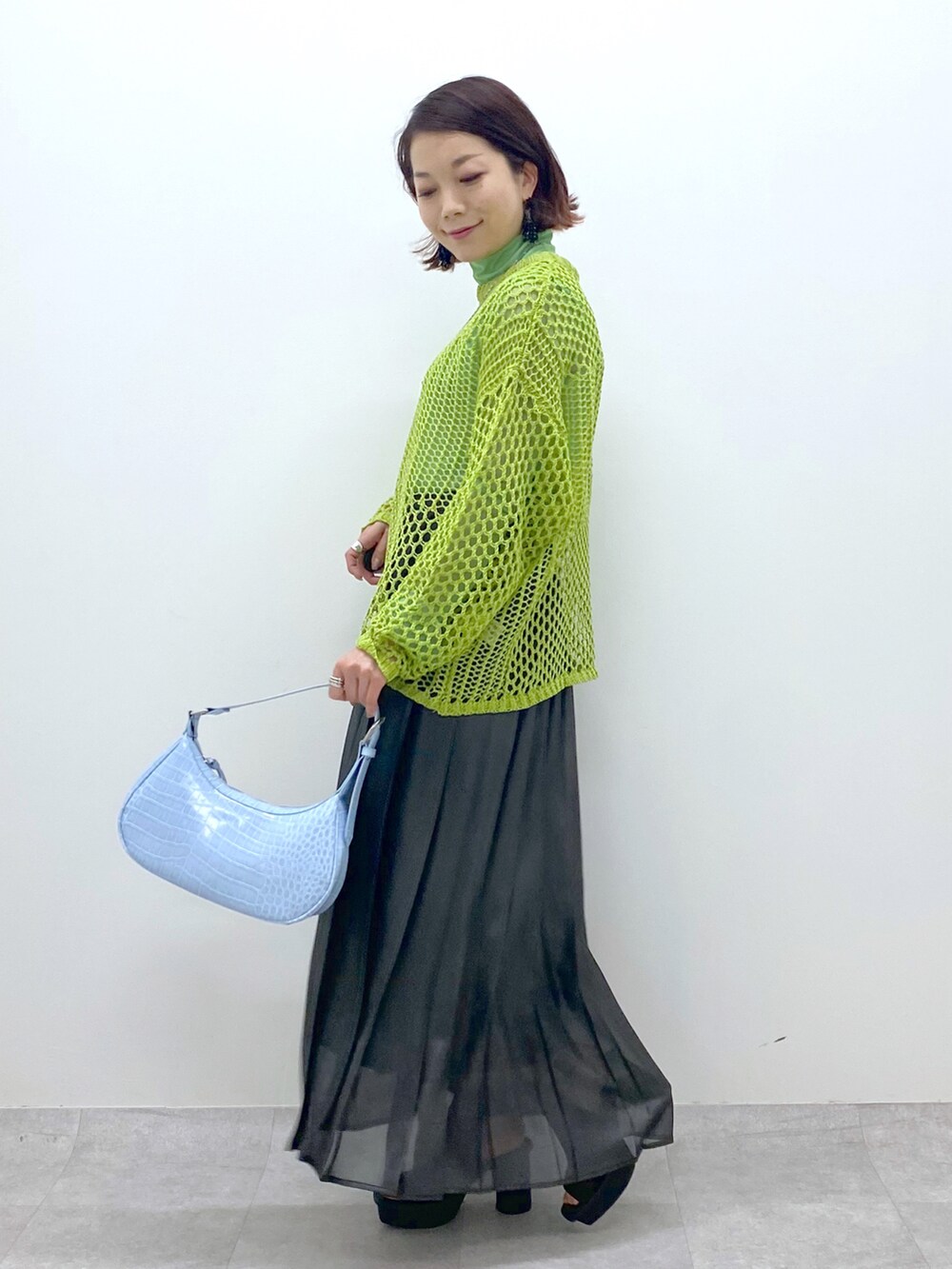 グリーン系のニット/セーター、グリーン系のTシャツ/カットソー、ブラック系のスカートを着用したレディースの春コーディネートの2枚目の写真