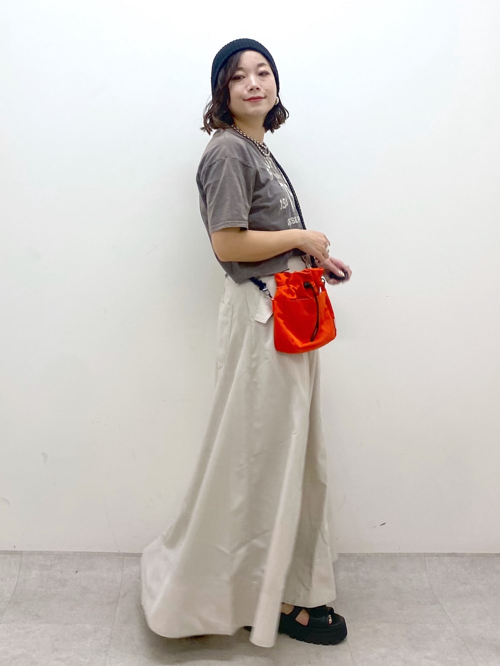 ブラック系のTシャツ/カットソー、オレンジ系のショルダーバッグ、ベージュ系のスカートを着用したレディースの夏コーディネートの5枚目の写真