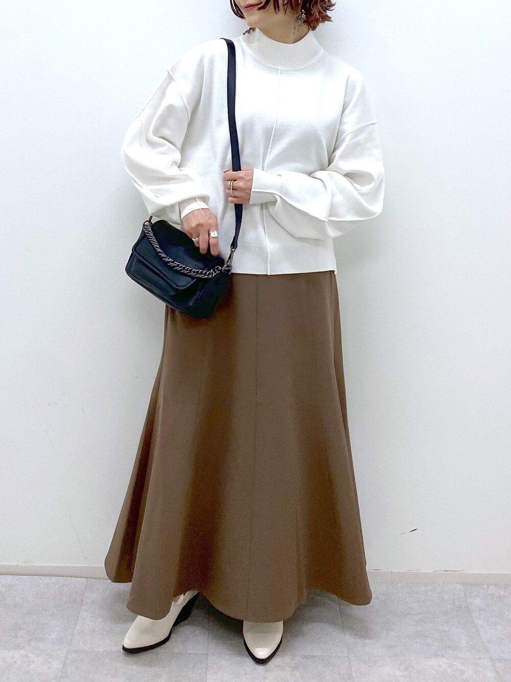 ホワイト系のブーツ、ブラウン系のスカート、ブラック系のバッグを着用したレディースの秋コーディネートの5枚目の写真