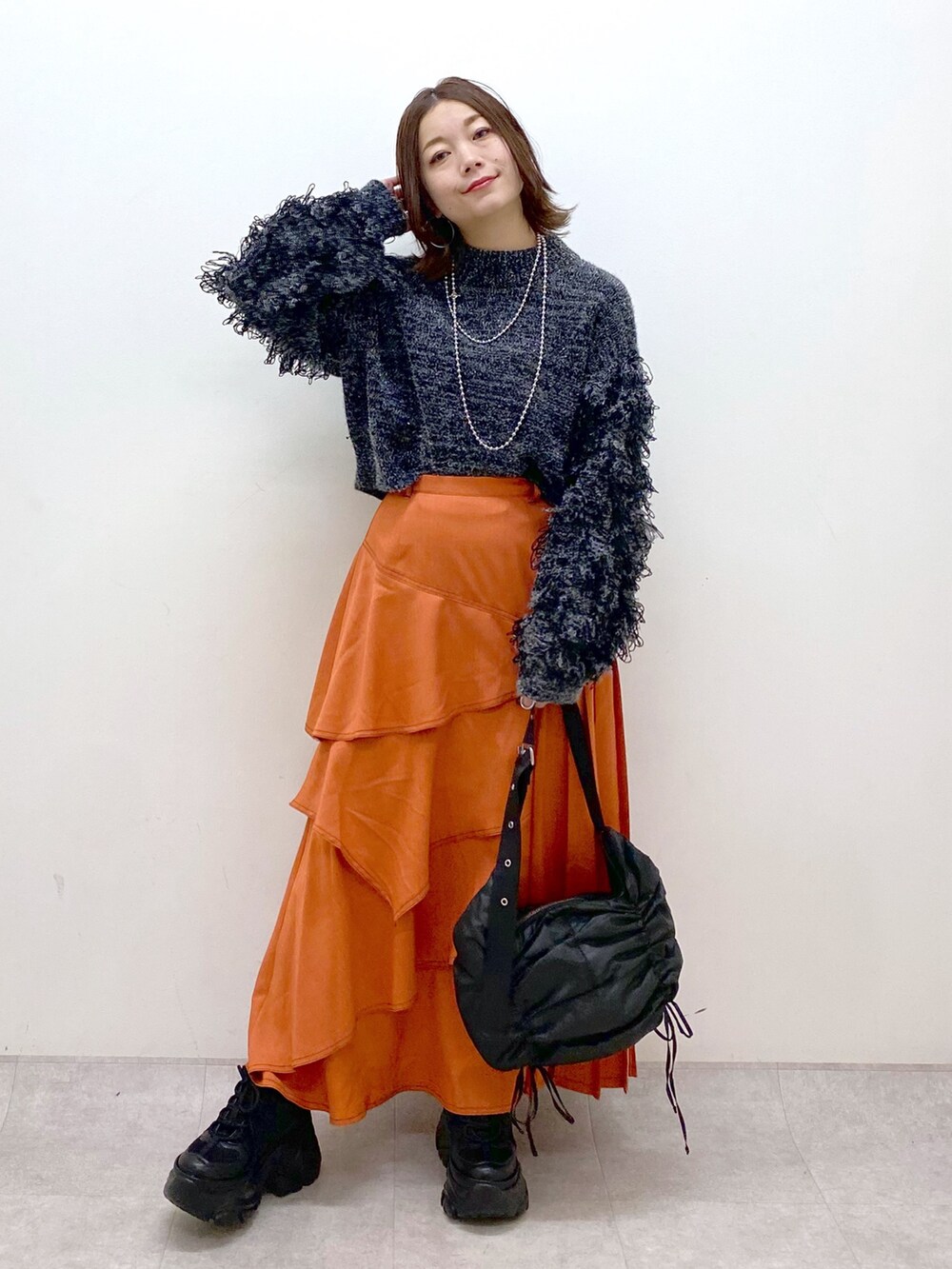 ブラック系のニット/セーター、オレンジ系のスカート、ブラック系のショルダーバッグを着用したレディースの冬コーディネートの9枚目の写真