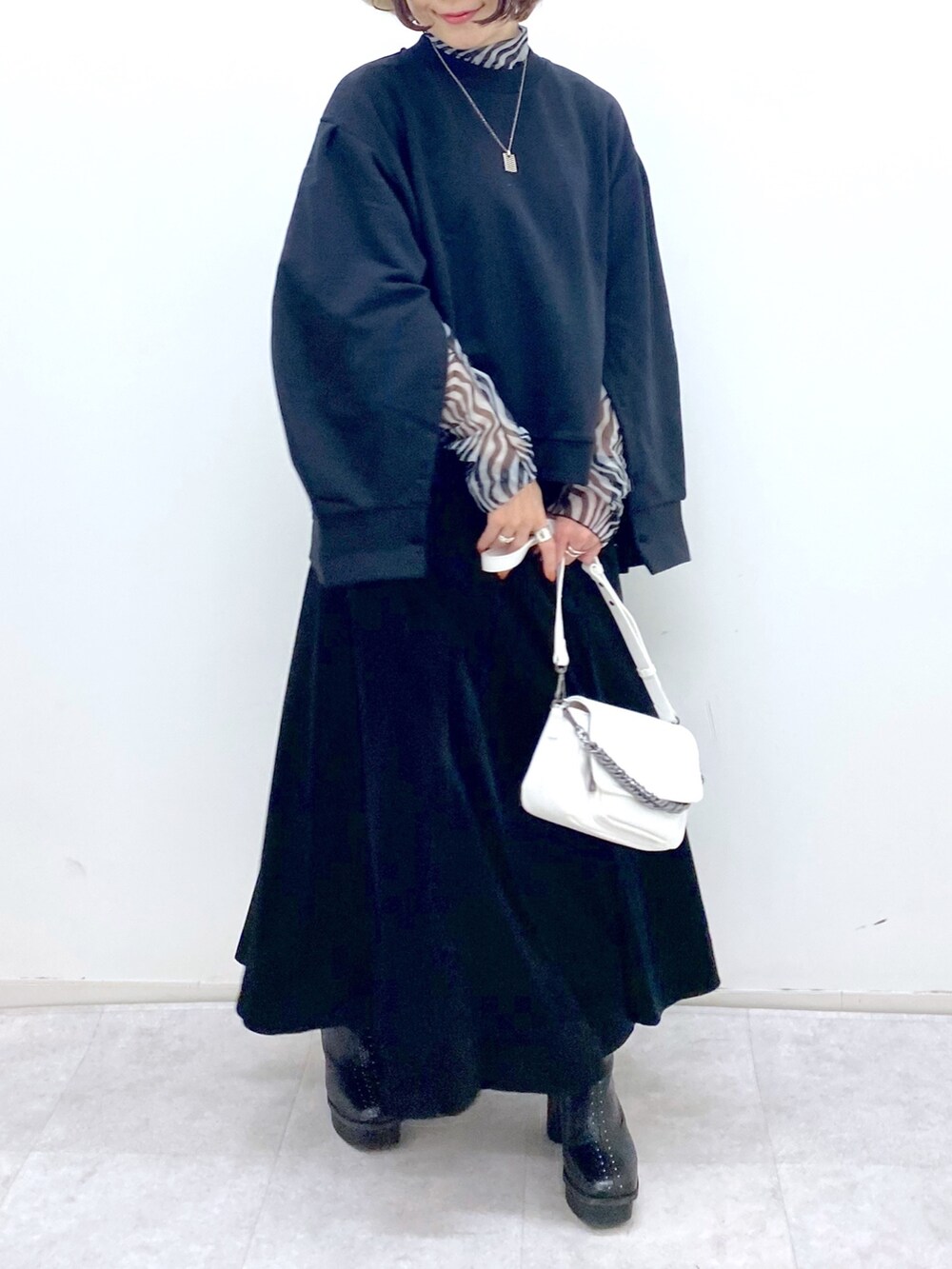 ブラック系のトップス、ホワイト系のバッグ、ブラック系のブーツを着用したレディースの秋コーディネートの5枚目の写真