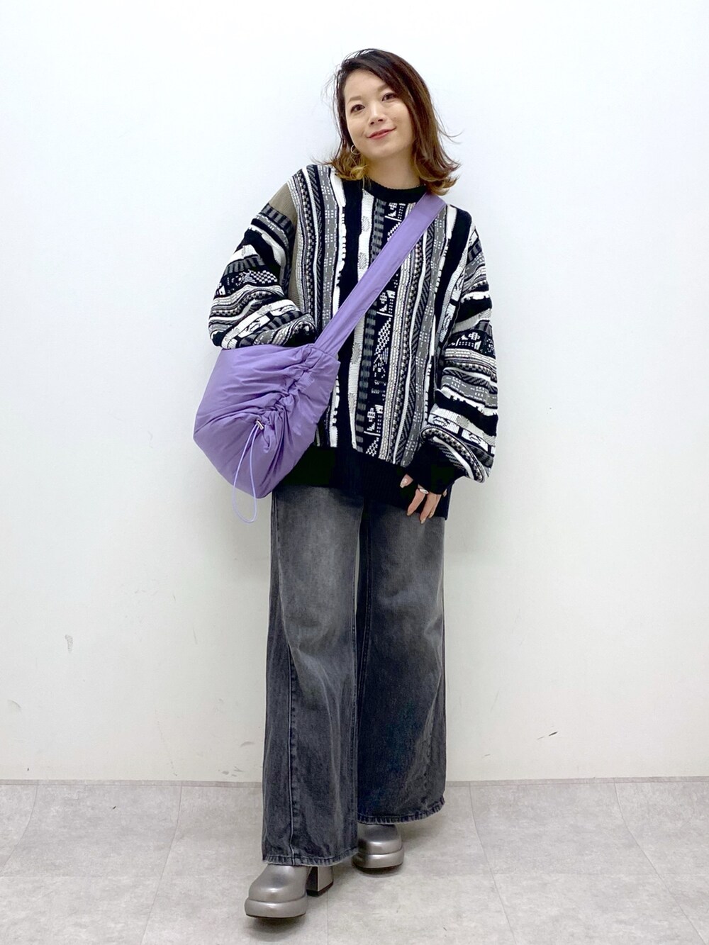 ブラック系のニット/セーター、ブラック系のデニムパンツ、パープル系のショルダーバッグを着用したレディースの秋コーディネートの2枚目の写真