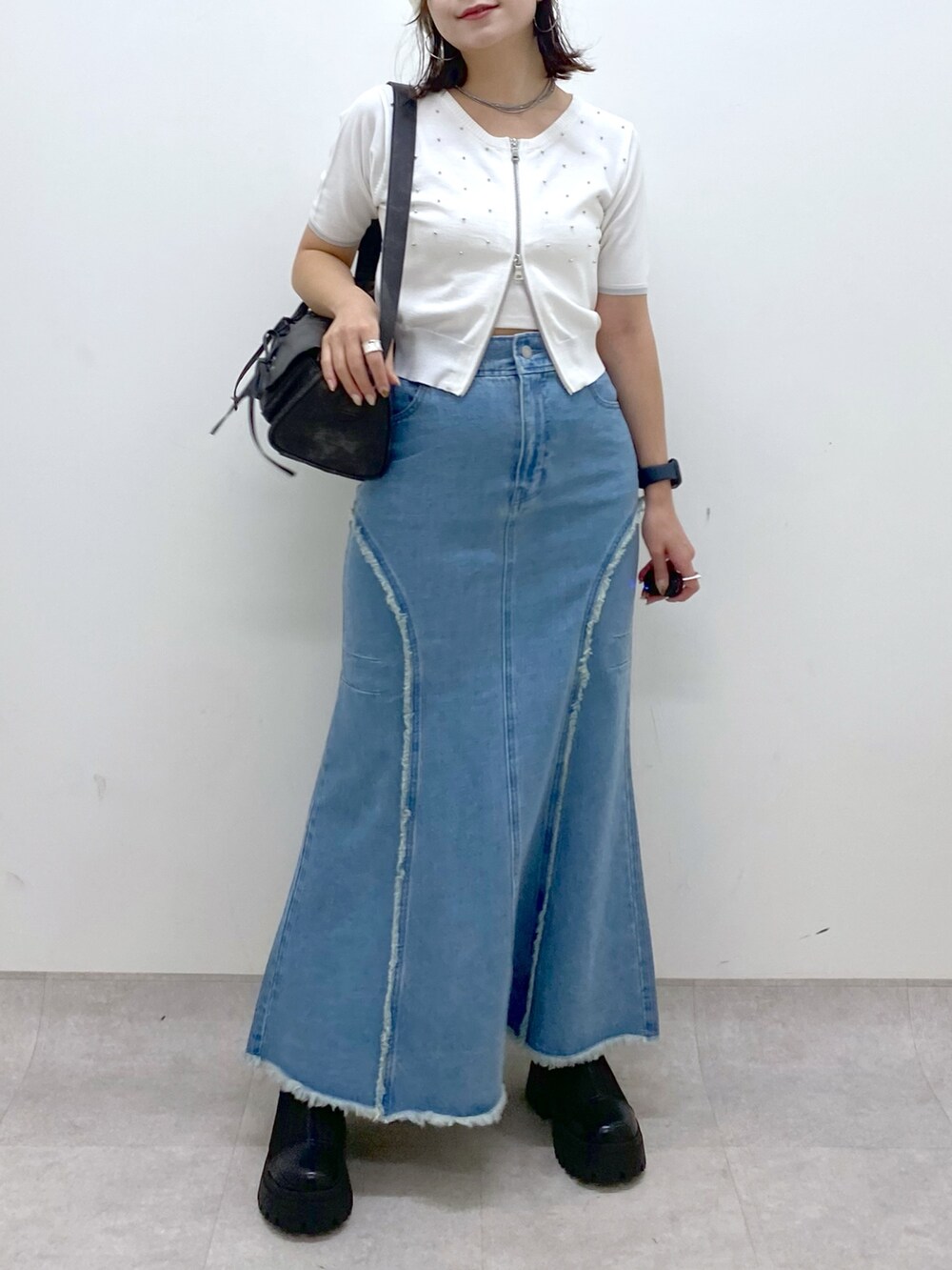 ブルー系のデニムスカート、ホワイト系のニット/セーター、ブラック系のショルダーバッグを着用したレディースの夏コーディネートの3枚目の写真