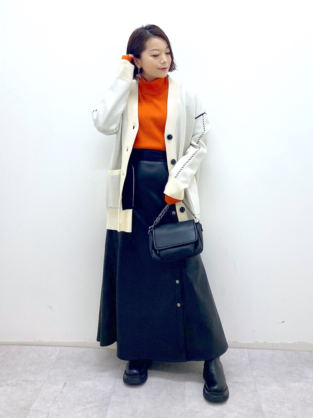 ブラック系のスカート、ブラック系のバッグ、オレンジ系のトップスを着用したレディースの秋コーディネートの2枚目の写真