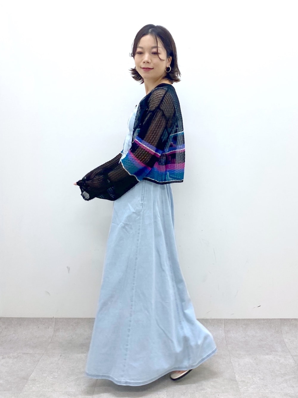 ブルー系のジャンパースカート、ホワイト系のサンダル、ブラック系のカーディガン/ボレロを着用したレディースの春コーディネートの2枚目の写真