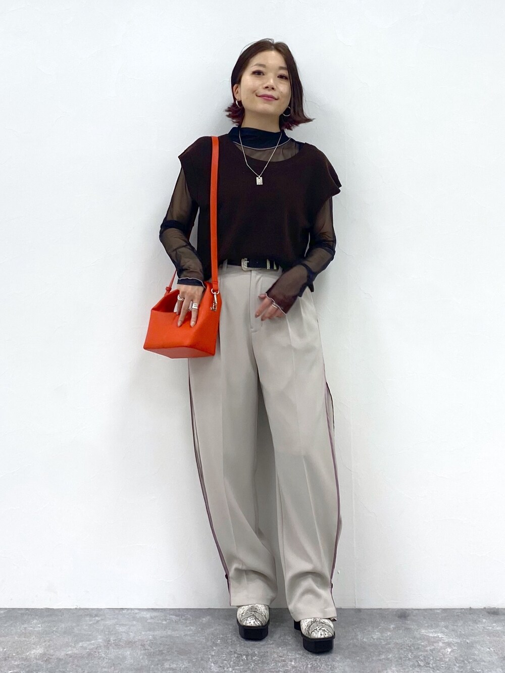 ベージュ系のスラックス、オレンジ系のショルダーバッグ、ブラウン系のワンピースを着用したレディースの夏コーディネートの5枚目の写真