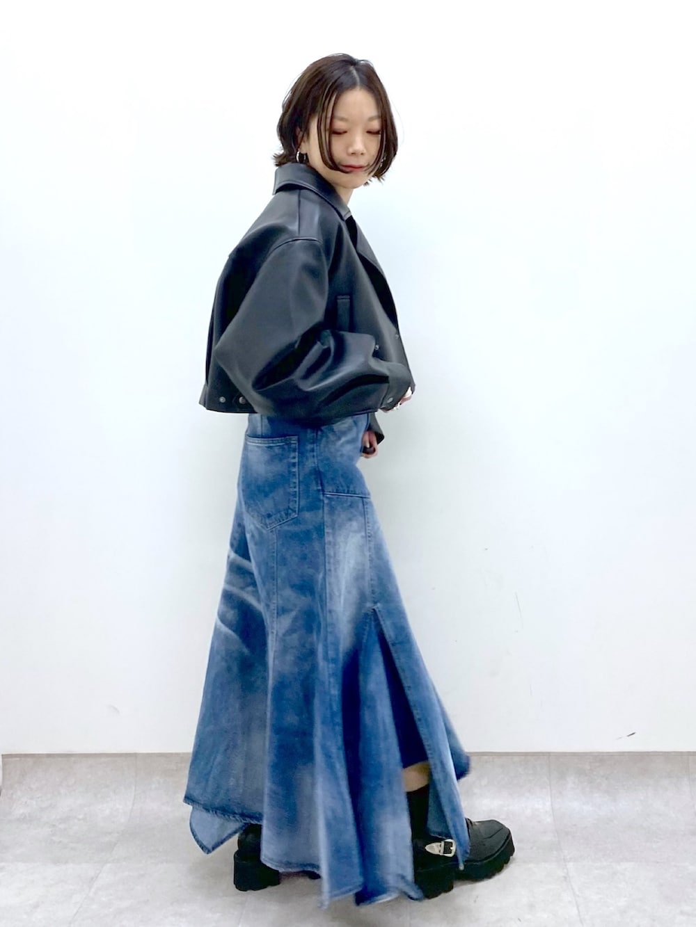 ブルー系のスカート、ブラック系のトップス、ブラック系のローファーを着用したレディースの春コーディネートの2枚目の写真