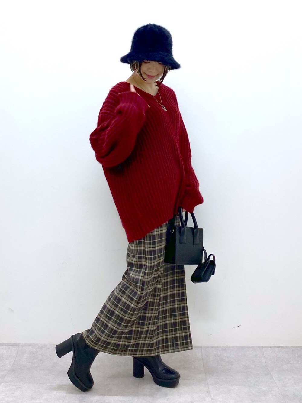 レッド系のニット/セーター、グリーン系のスカート、ブラック系のブーツを着用したレディースの冬コーディネートの2枚目の写真