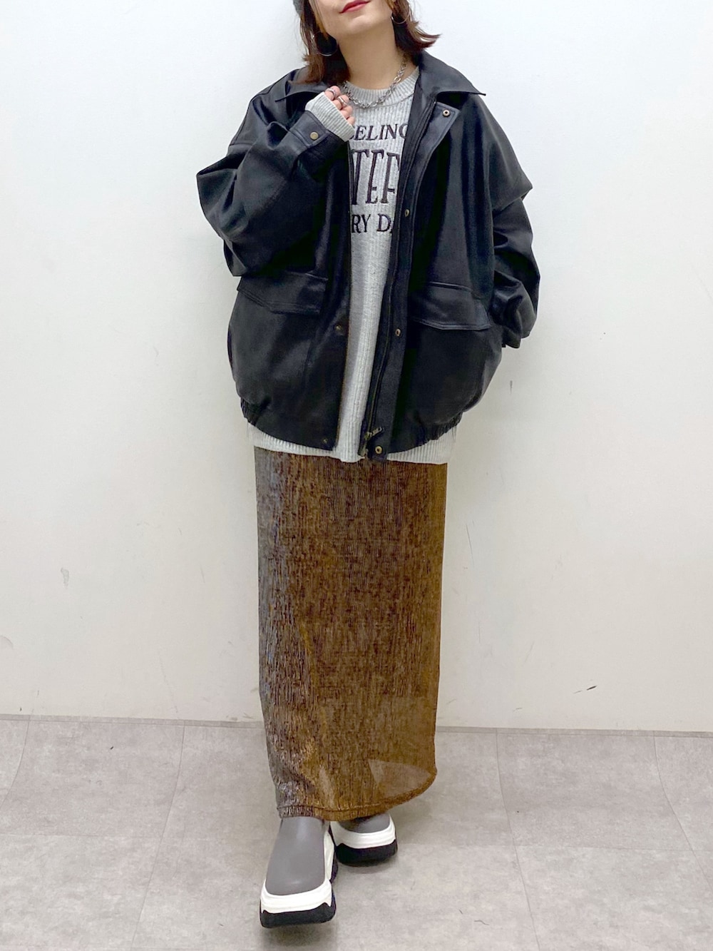 グレー系のニット/セーター、ブラック系のブルゾン、ゴールド系のスカートを着用したレディースの秋コーディネートの3枚目の写真