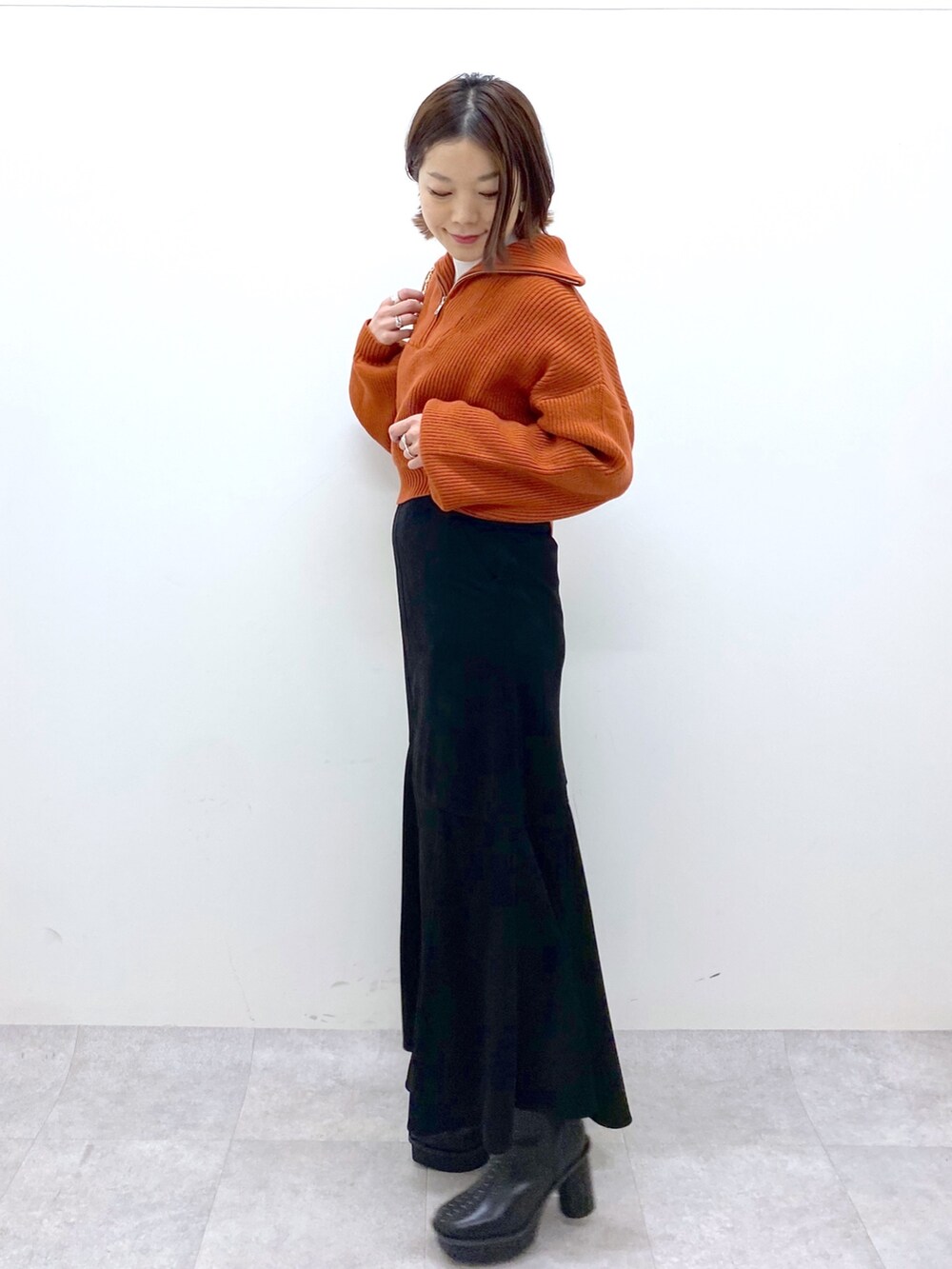 ブラック系のスカート、ホワイト系のバッグ、オレンジ系のニット/セーターを着用したレディースの秋コーディネートの2枚目の写真