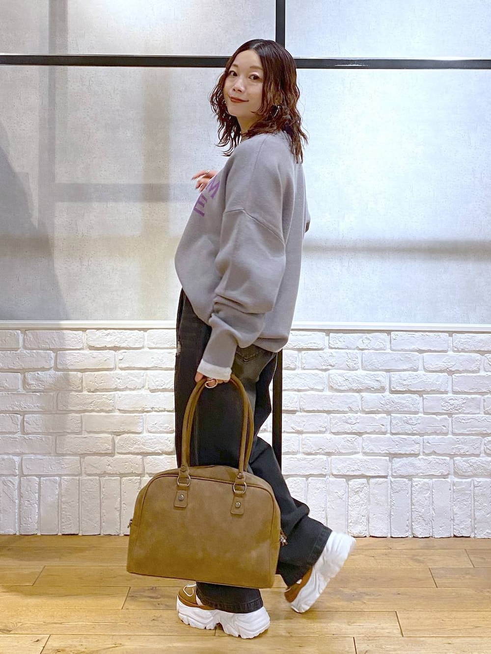 ベージュ系のスニーカー、イエロー系のボストンバッグ、ブラック系のデニムパンツを着用したレディースの秋コーディネートの5枚目の写真