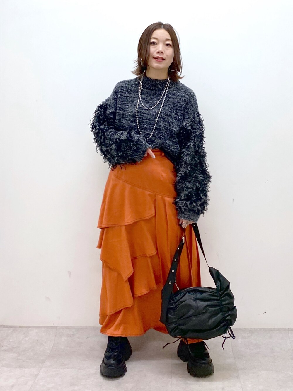 ブラック系のニット/セーター、オレンジ系のスカート、ブラック系のショルダーバッグを着用したレディースの冬コーディネートの4枚目の写真