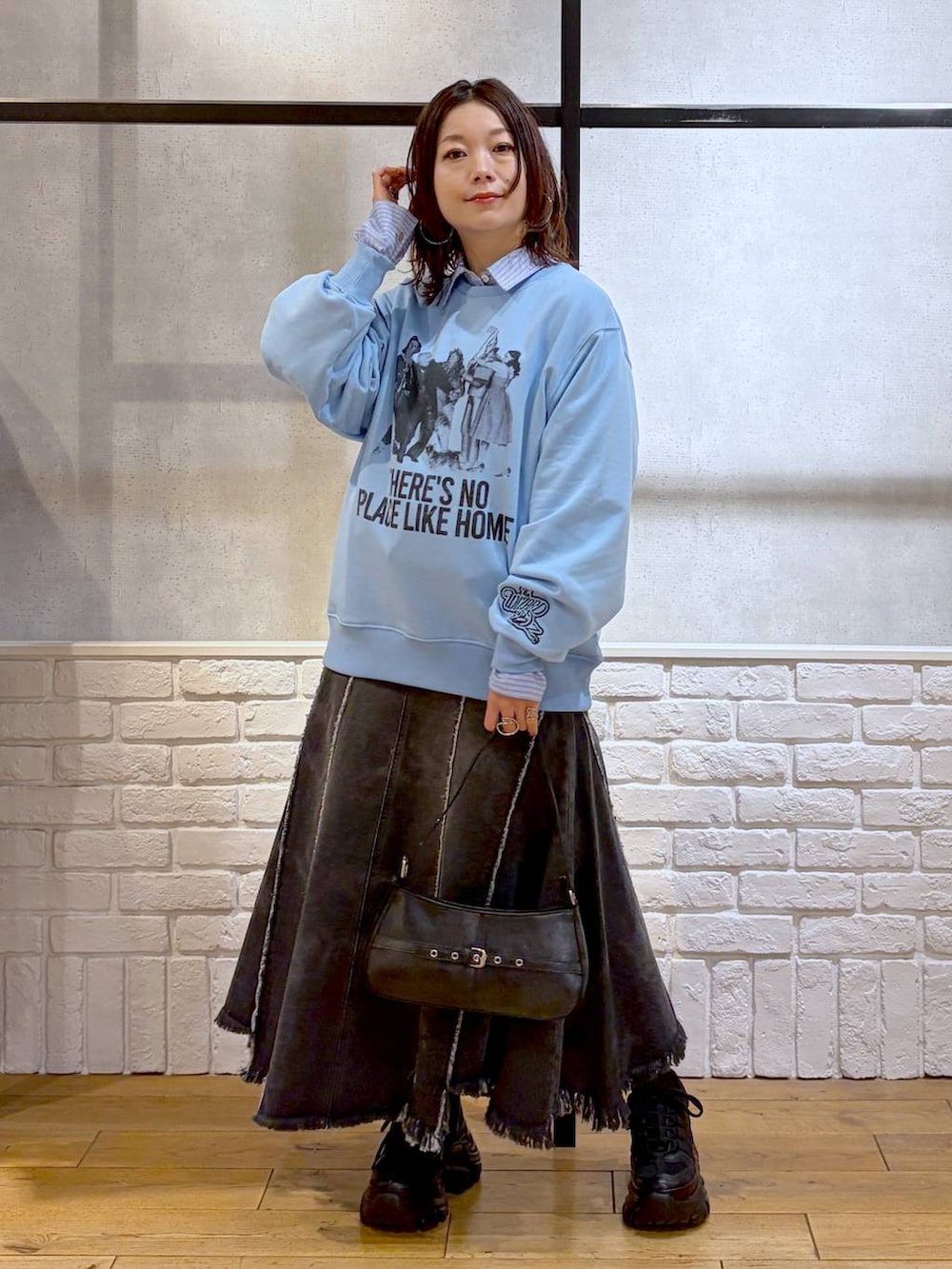 ブラック系のスニーカー、ブラック系のハンドバッグ、ブラック系のデニムスカートを着用したレディースの春コーディネートの4枚目の写真