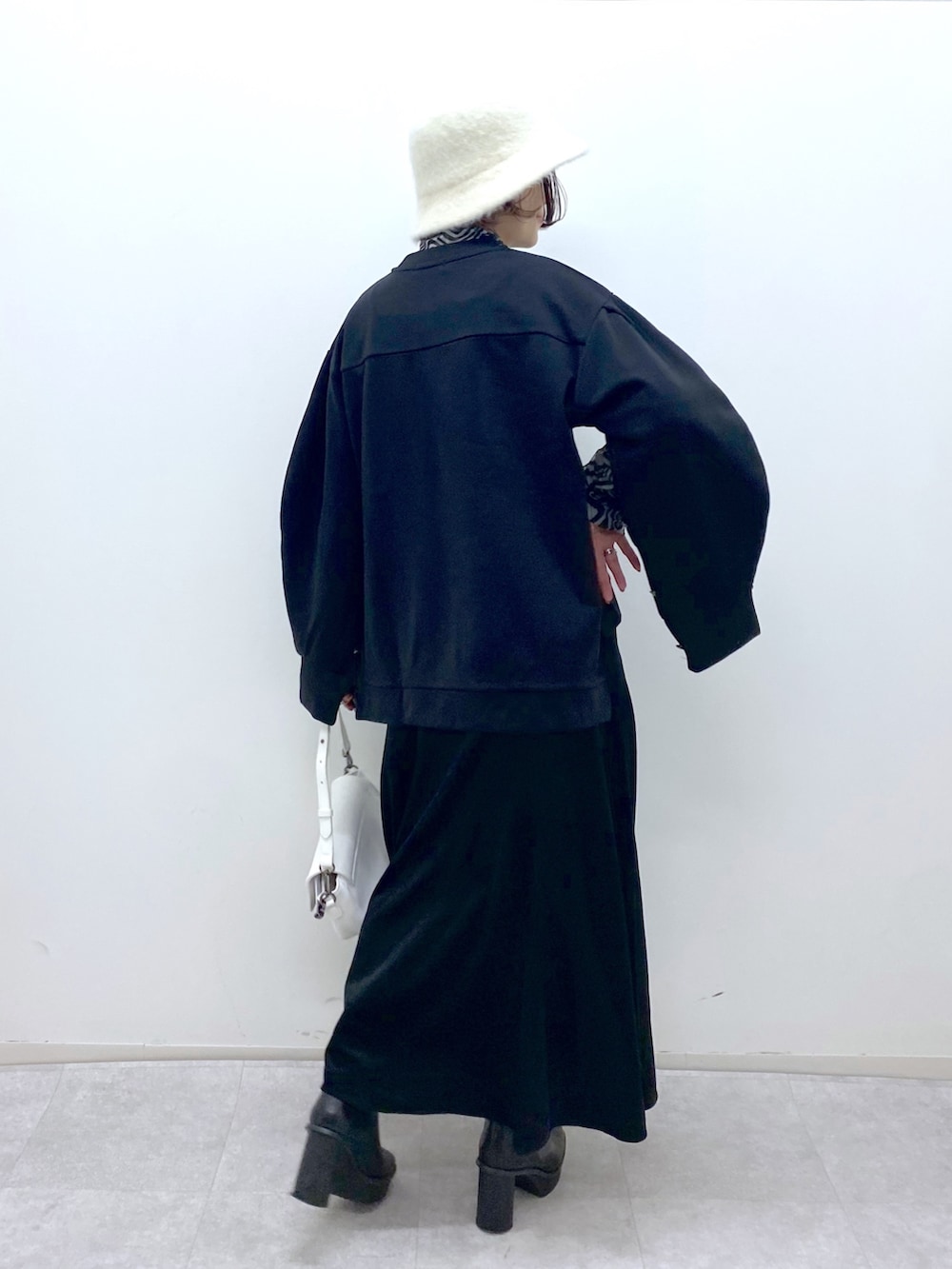 ブラック系のトップス、ホワイト系のバッグ、ブラック系のブーツを着用したレディースの秋コーディネートの4枚目の写真