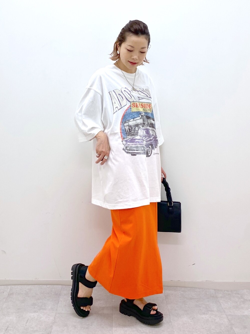 ホワイト系のTシャツ/カットソー、オレンジ系のスカート、ブラック系のショルダーバッグを着用したレディースの夏コーディネートの5枚目の写真