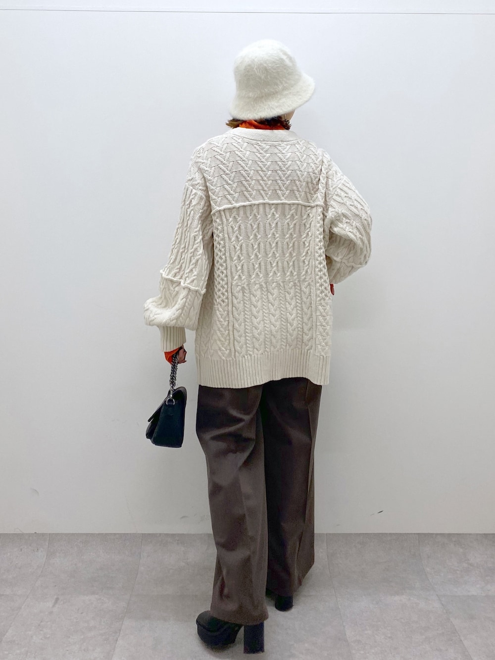 オレンジ系のトップス、ブラック系のバッグ、ブラック系のブーツを着用したレディースの秋コーディネートの3枚目の写真