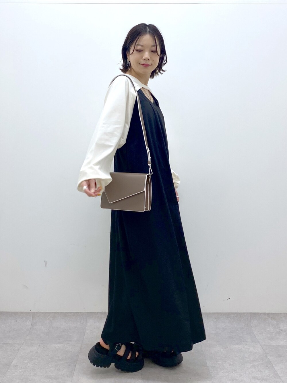 ブラック系のジャンパースカート、ホワイト系のTシャツ/カットソー、ブラウン系のショルダーバッグを着用したレディースの春コーディネートの2枚目の写真
