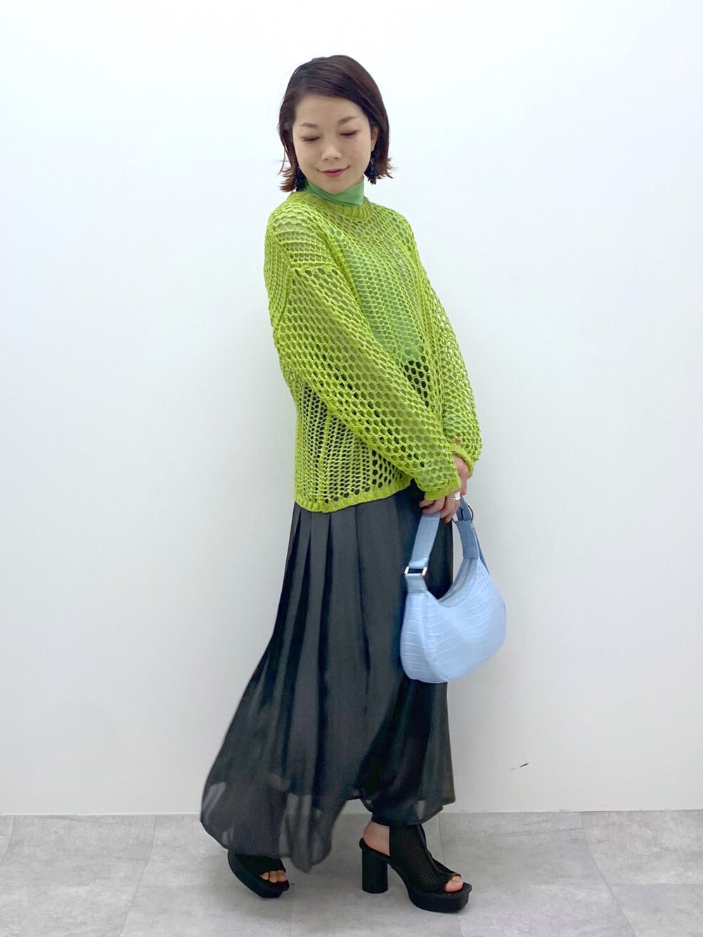 グリーン系のニット/セーター、グリーン系のTシャツ/カットソー、ブラック系のスカートを着用したレディースの春コーディネートの5枚目の写真