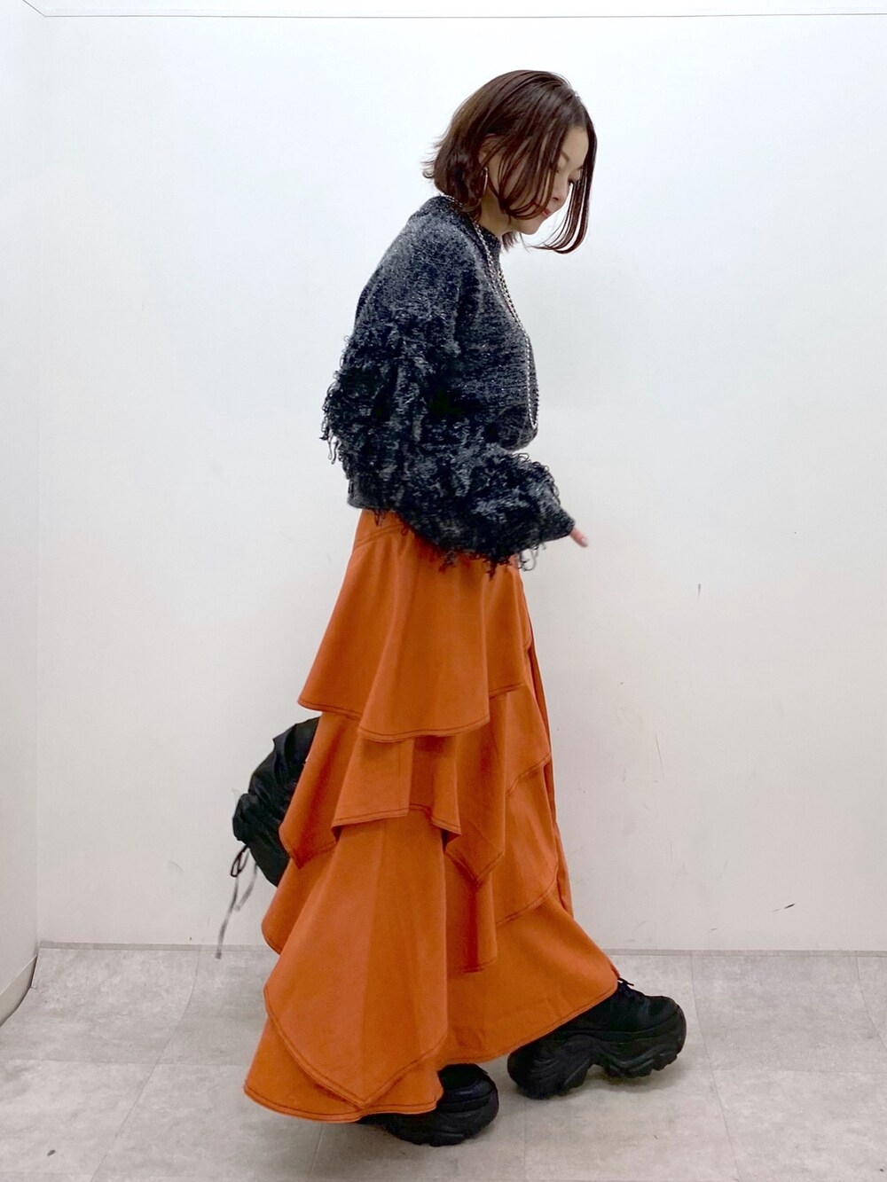 ブラック系のニット/セーター、オレンジ系のスカート、ブラック系のショルダーバッグを着用したレディースの冬コーディネートの7枚目の写真
