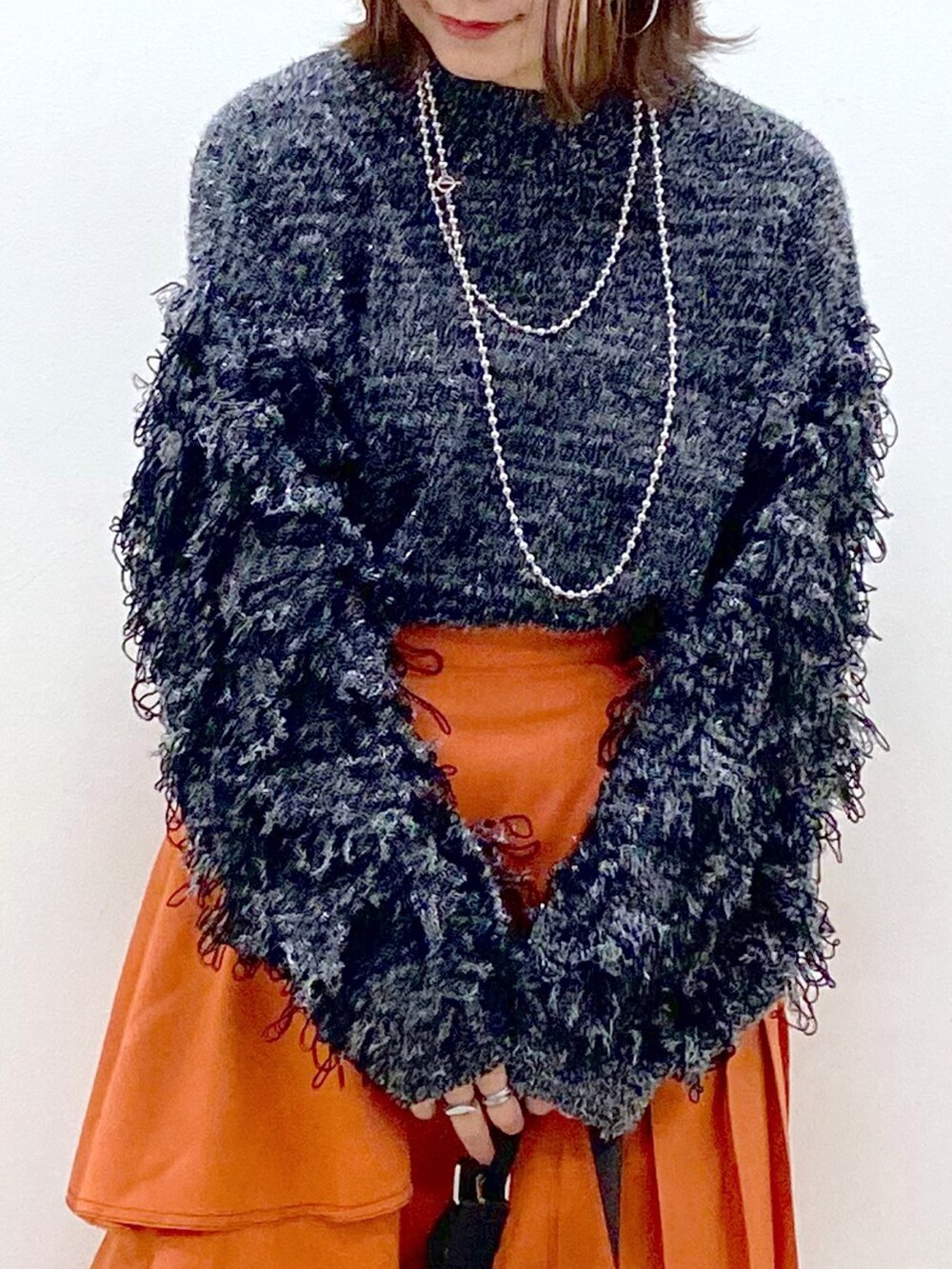 ブラック系のニット/セーター、オレンジ系のスカート、ブラック系のショルダーバッグを着用したレディースの冬コーディネートの2枚目の写真