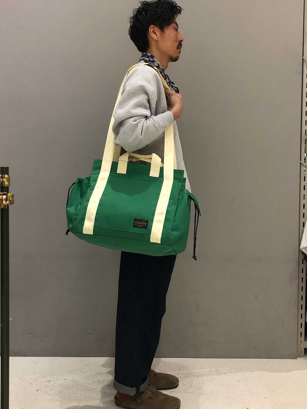 グレー系のスウェット、ブルー系のデニムパンツ、グリーン系のトートバッグを着用したメンズの冬コーディネートの3枚目の写真