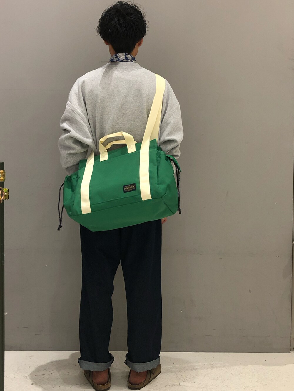 グレー系のスウェット、ブルー系のデニムパンツ、グリーン系のトートバッグを着用したメンズの冬コーディネートの2枚目の写真