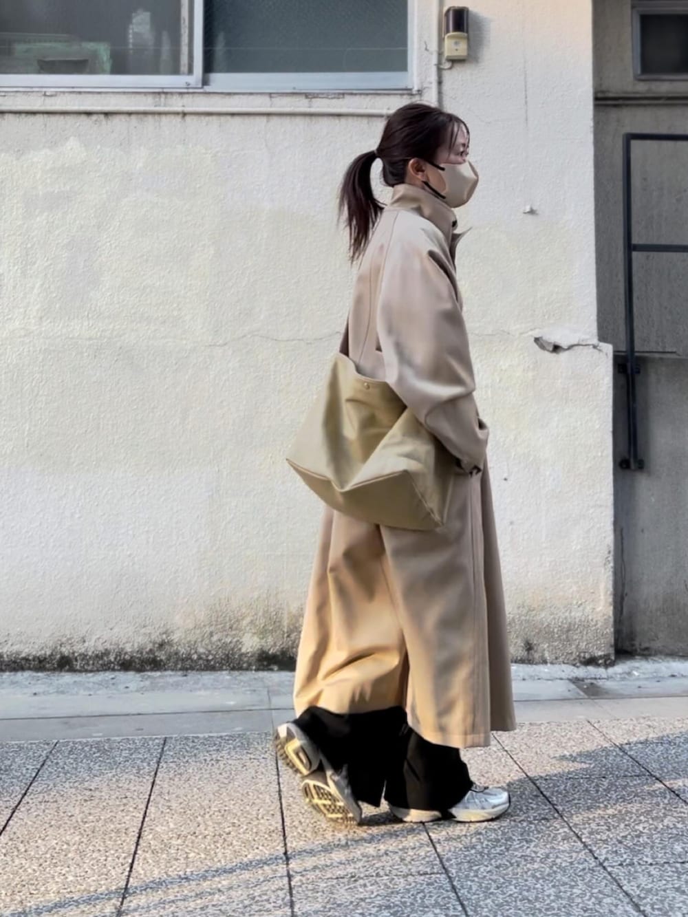 ベージュ系のステンカラーコート、ベージュ系のショルダーバッグ、ブラック系のその他パンツを着用したレディースの春コーディネートの2枚目の写真